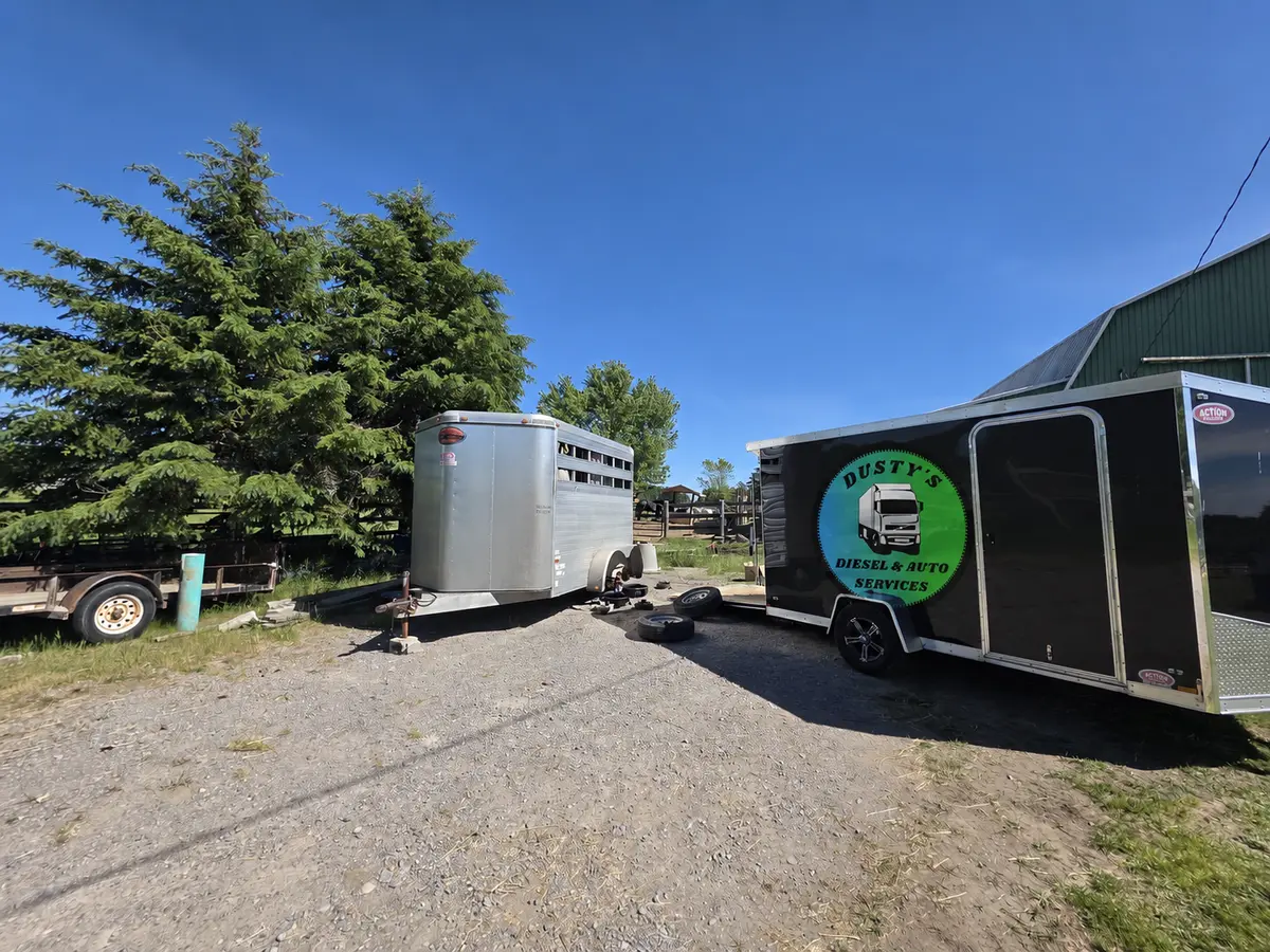 Dusty's black service trailer parked on a gravel farm yard beside a customer's livestock trailer